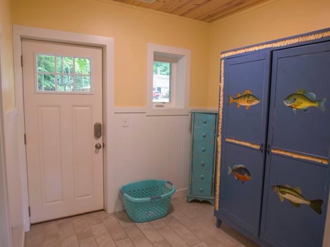 Mudroom with yellow walls, white door with glass panels, turquoise storage basket, green shelving unit, and blue cabinet with hand-painted fish designs