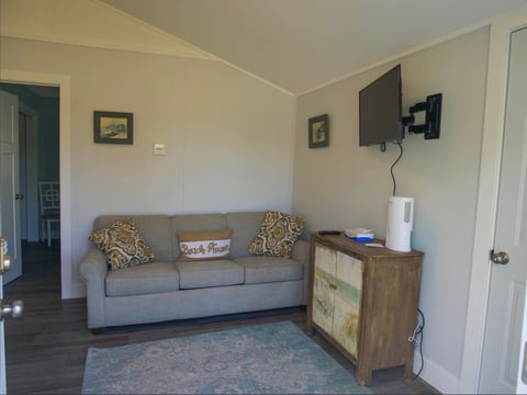Living room with gray sofa, patterned pillows, wooden cabinet, wall-mounted TV, and beige walls