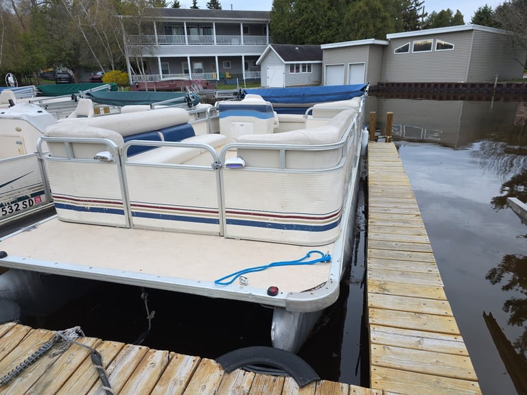 Pontoon boats docked at a wooden pier with residential houses and trees in the background