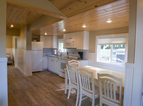 Bright modern kitchen and dining area with wood ceiling, white appliances, dining table with chairs, and natural light from windows