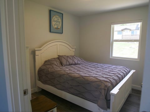 Bedroom with white wooden bed featuring dark gray bedding, pale green walls, window, and framed artwork above headboard