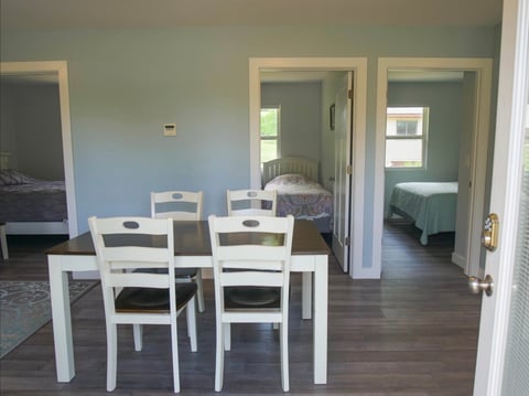 Spacious room with white dining table and chairs, hardwood floors, and doorways leading to bedrooms with visible beds