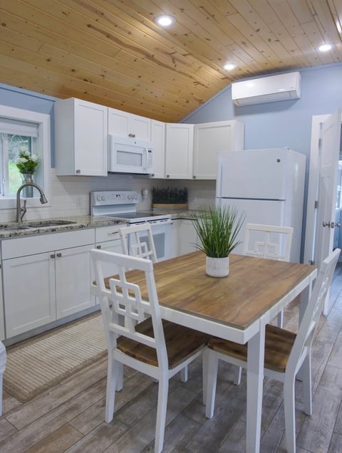 Bright kitchen with white cabinets, wood ceiling, and light blue walls featuring a wooden dining table with white chairs