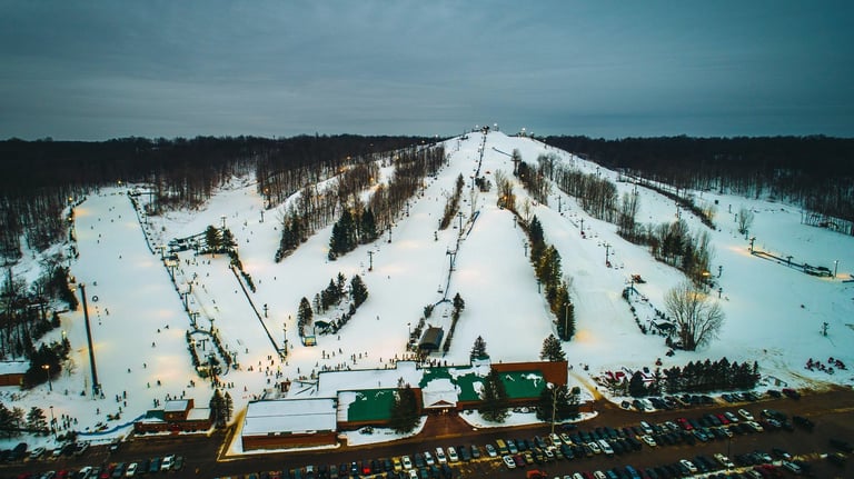 Aerial view of a ski resort with snow-covered slopes, ski lifts, and forested areas on an overcast winter day