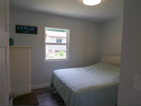 Minimalist bedroom with single bed, window, white walls, closet door, and Hamlin neon sign on wall